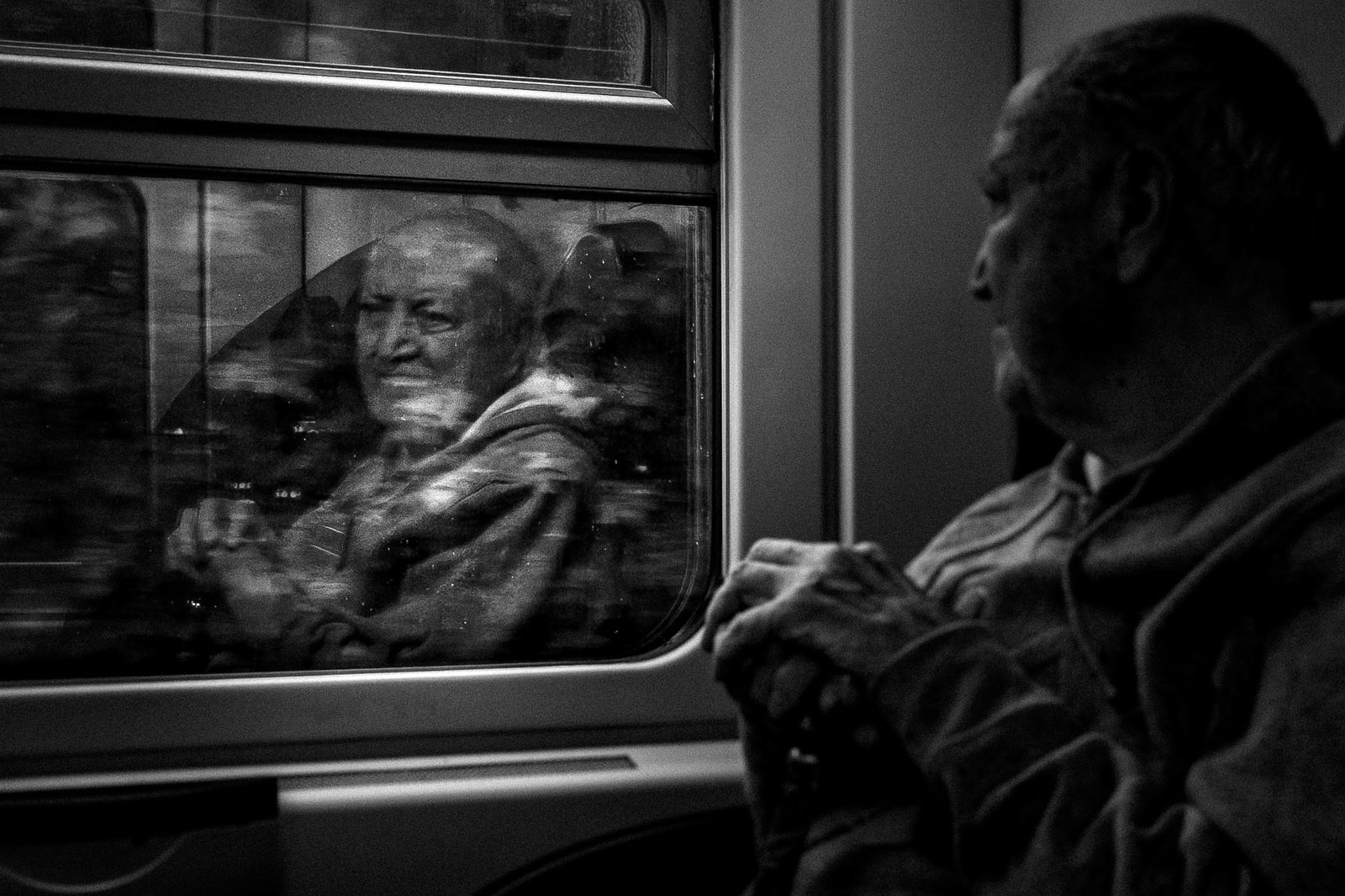Un uomo sul treno e un volto riflesso nel finestrino