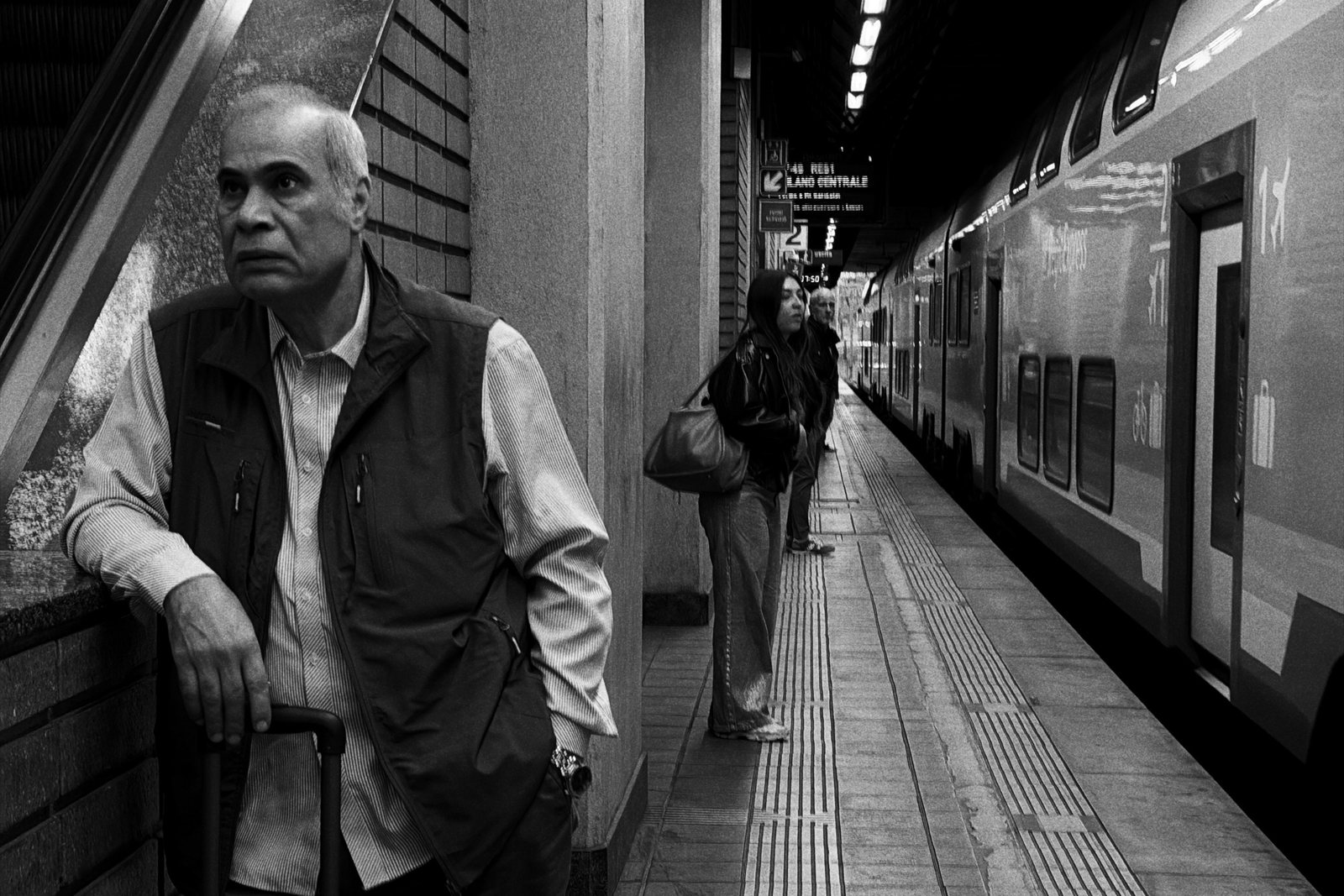 Un uomo anziano appoggiato a un pilastro accanto al treno