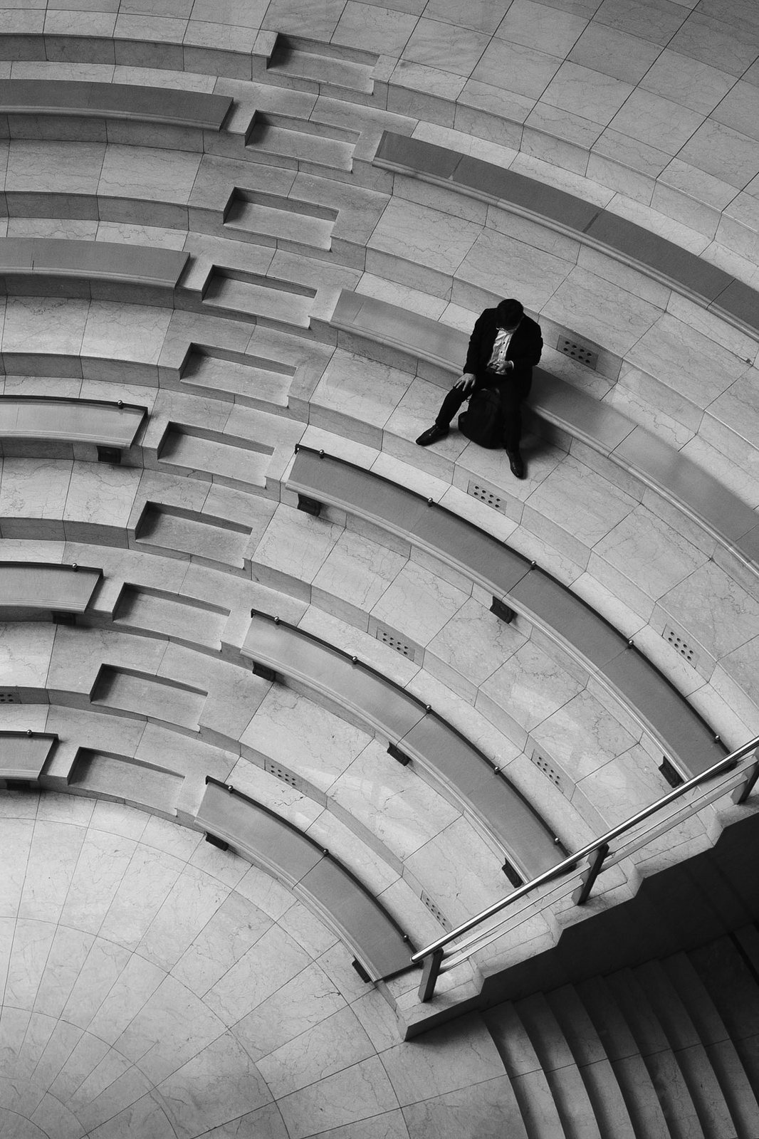 Una persona seduta sui gradini curvi di una scala, vista dall'alto